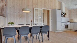 A modern kitchen with wooden walls, a dining area with a table and chairs, and a built-in oven and refrigerator. - "Bentine" - 1.6km from the sea by Interhome (Saltum)