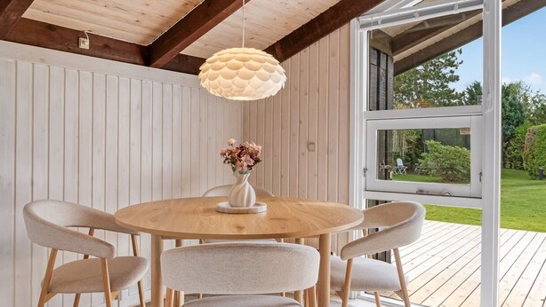 Une table ronde en bois, entourée de six chaises, un vase rempli de fleurs et un luminaire au design original suspendu au plafond.