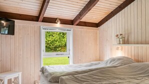 Une chambre à coucher avec un lit, une petite table blanche, une fenêtre donnant sur un paysage verdoyant et des murs en bois.