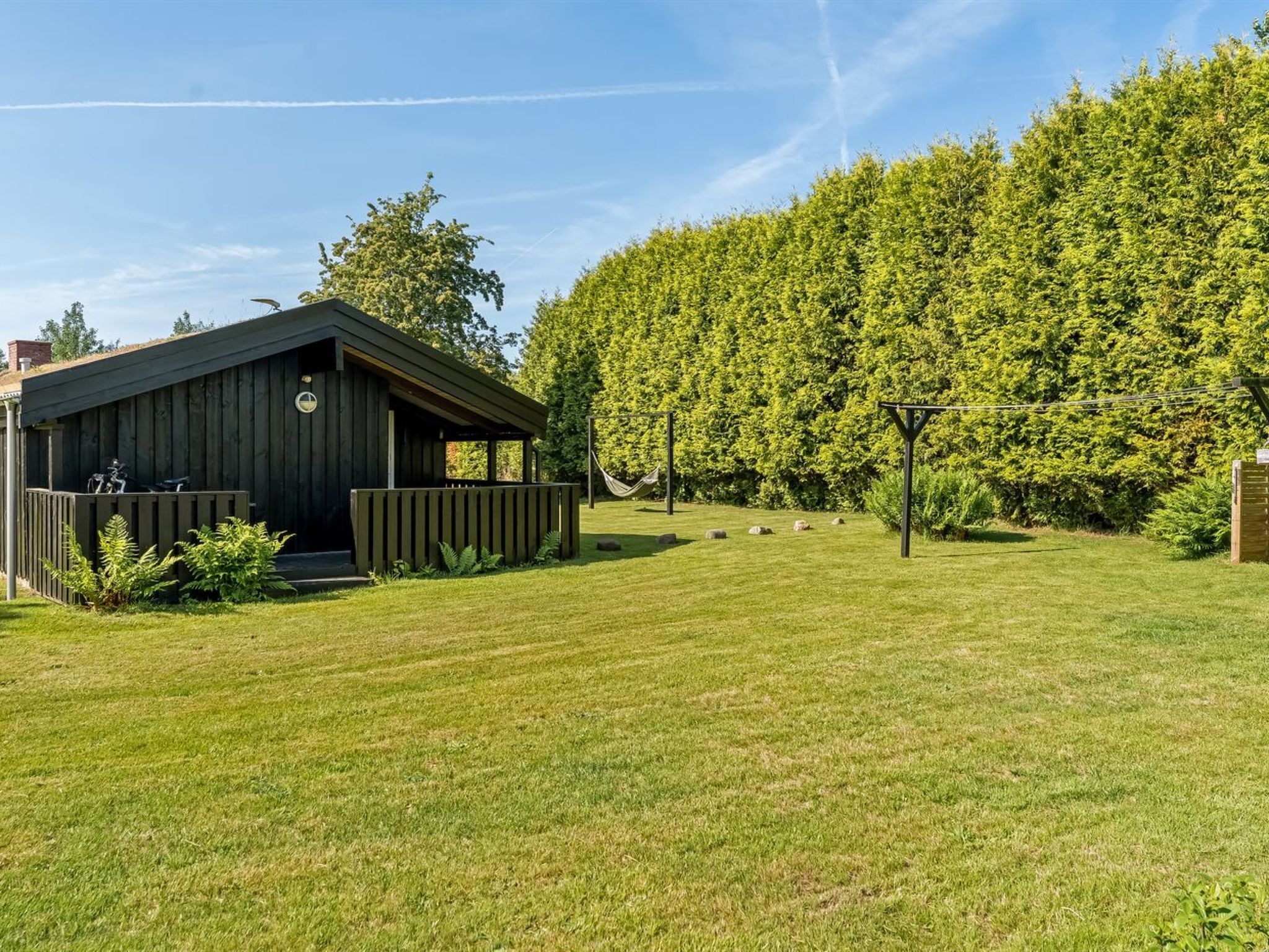 Ein von einer Hecke umgebener Außenbereich mit einem Holzhaus und einer Hängematte.