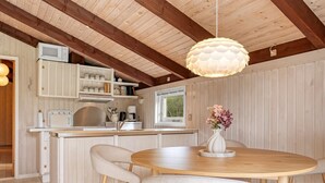 Une cuisine moderne avec des meubles blancs, une table à manger en bois et quatre chaises, ainsi qu’un luminaire suspendu.