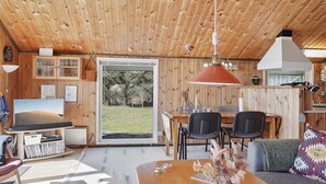 Interior acogedor de una cabaña con techo de madera, una zona de comedor, una sala de estar con sofá y televisor sobre un mueble de madera.