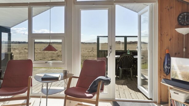 Una habitación con dos sillas rojas, una mesita y un ventanal con vistas a un campo.