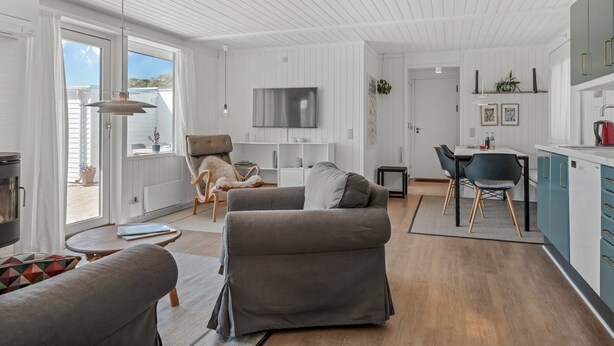 Una sala de estar moderna con un sofá, una silla, un televisor y un comedor con mesa y sillas.
