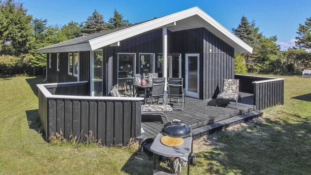 Eine moderne Hütte mit einer Terrasse, einem Grill und einem Essbereich mit Gartenmöbeln.