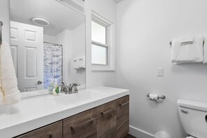 Un baño moderno con un tocador blanco, un espejo grande, una ducha con cortina azul y un inodoro.