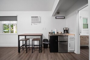 Una cocina compacta con una mesa de madera, dos taburetes, un refrigerador y una cafetera.
