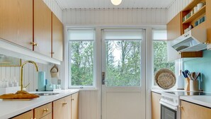 Eine moderne Küche mit Holzausstattung, einer weißen Arbeitsplatte, einem eingebauten Backofen und einem großen Fenster mit Blick auf Bäume.