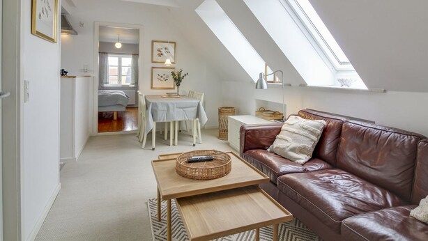 A spacious loft apartment with a high ceiling, skylights, a cozy brown leather sofa, a dining area with a table and chairs, and a kitchen in the background. - "Evangelina" - 350m from the sea by Interhome (Løkken)