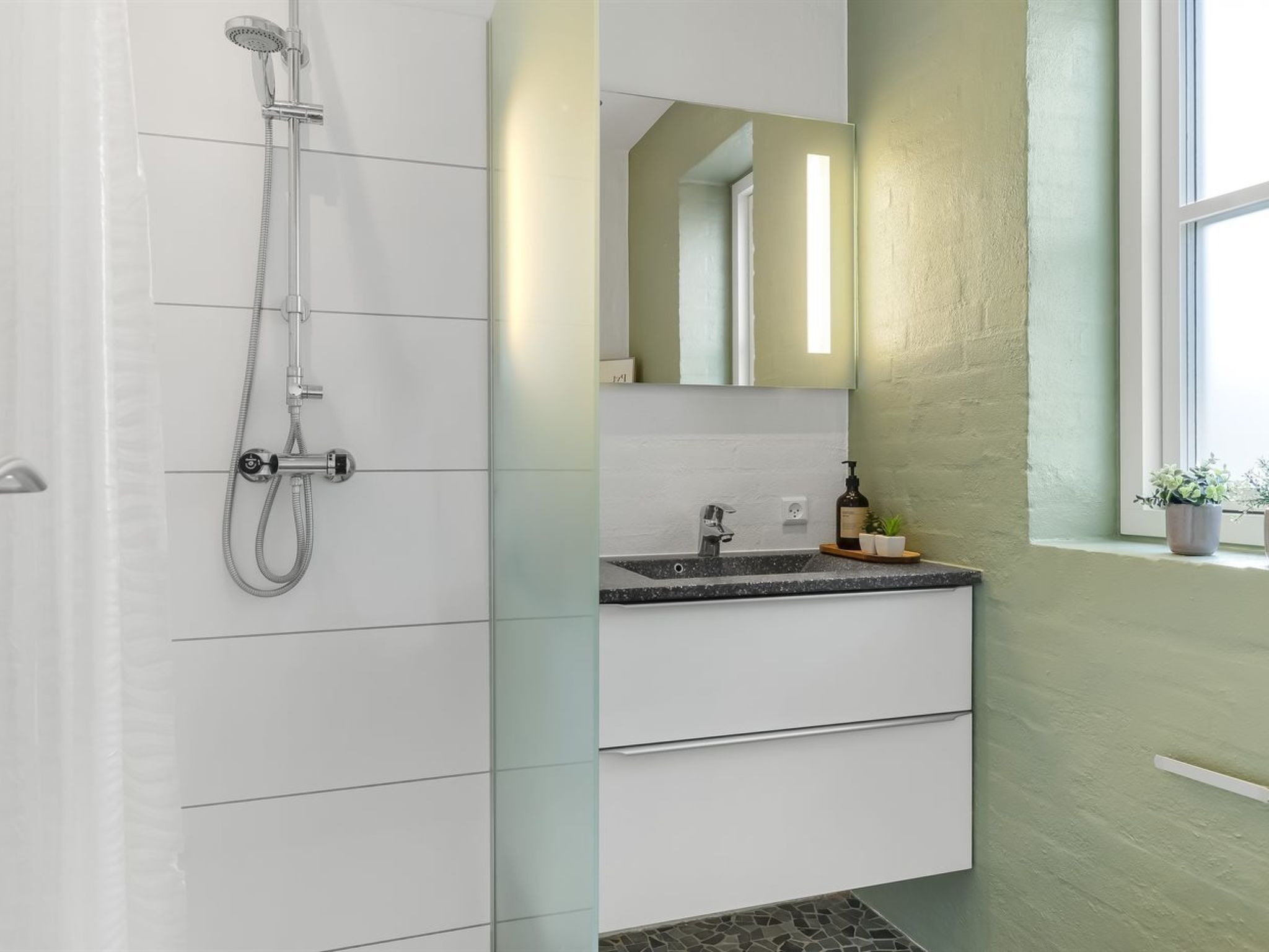 Un baño moderno con ducha, lavabo con espejo y ventana con plantas.