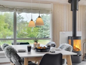 Een gezellige eethoek met een gedekte tafel voor twee, een houtkachel en uitzicht op groen.