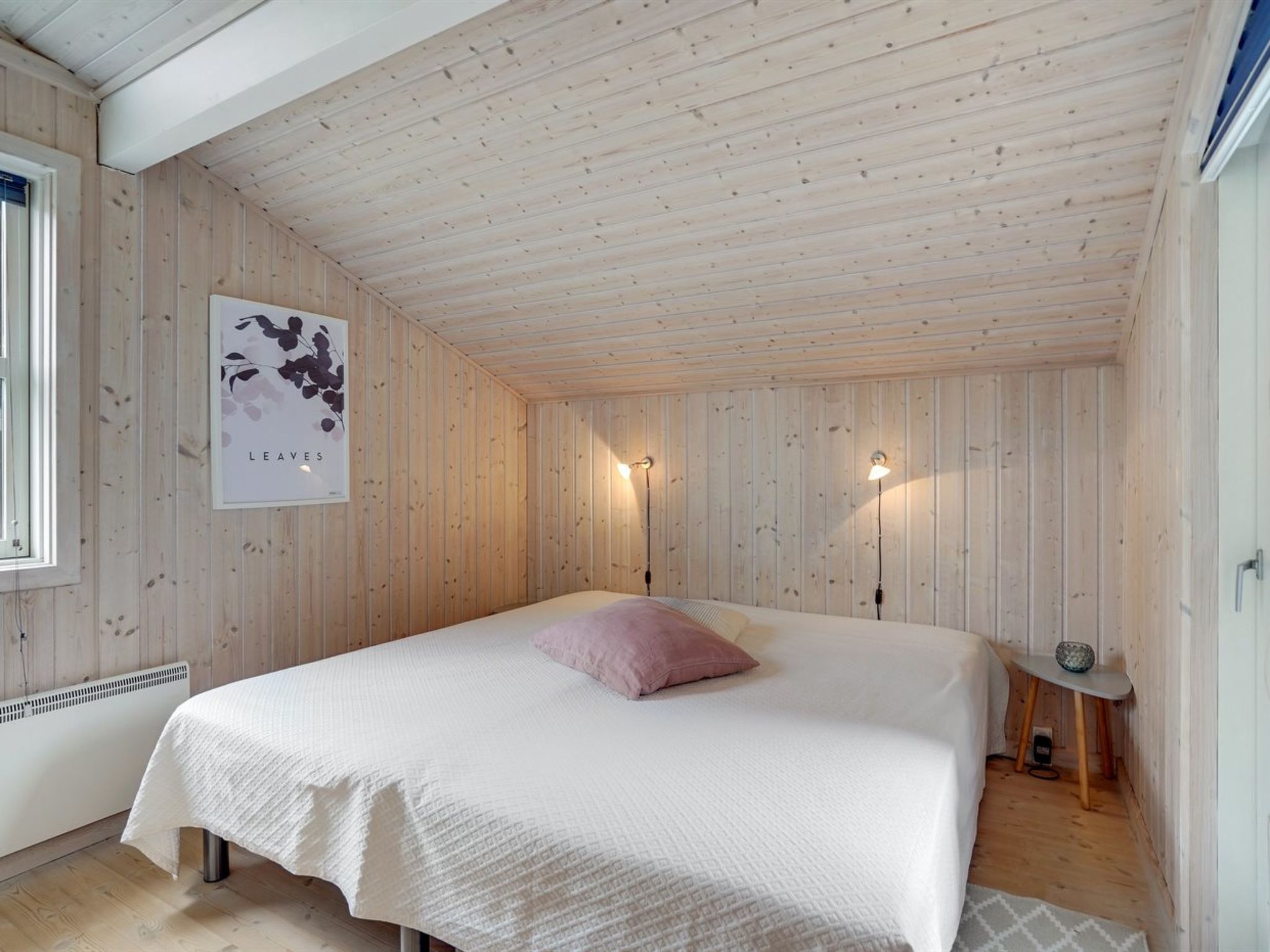 Quarto aconchegante com uma cama grande, paredes de madeira e duas luminárias fixadas na parede.
