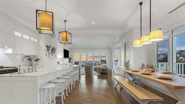A modern kitchen with white cabinetry, a central island with bar stools, and a dining area with a long table set for six.