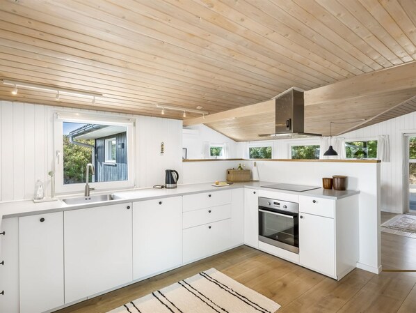 A modern kitchen with white cabinetry, a built-in oven, and a wooden ceiling.