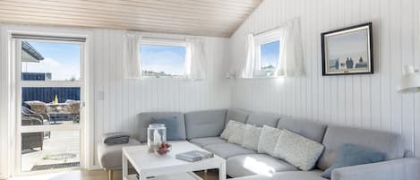 Un salon moderne avec un canapé gris, une table basse blanche et une vue sur l’extérieur grâce à une porte coulissante.