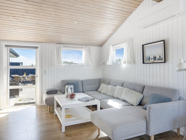 Una sala de estar moderna con un sofá gris, una mesa de centro blanca y vistas al exterior a través de un ventanal corredizo.