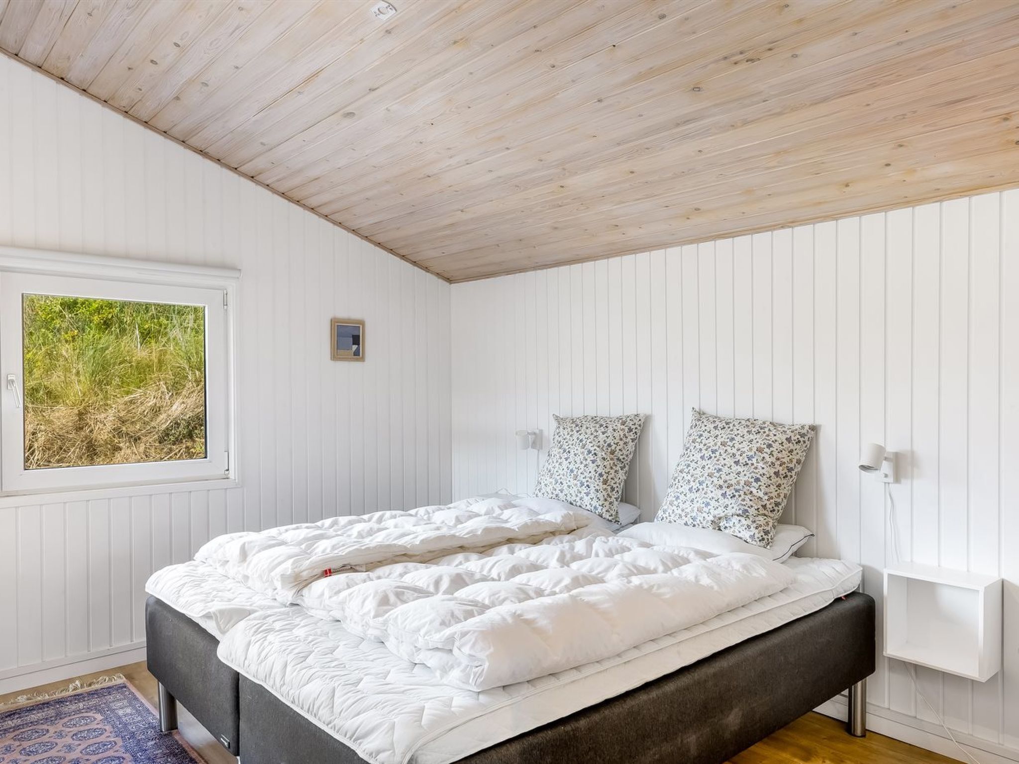 A bedroom with a bed, a window, and a wall-mounted light fixture.