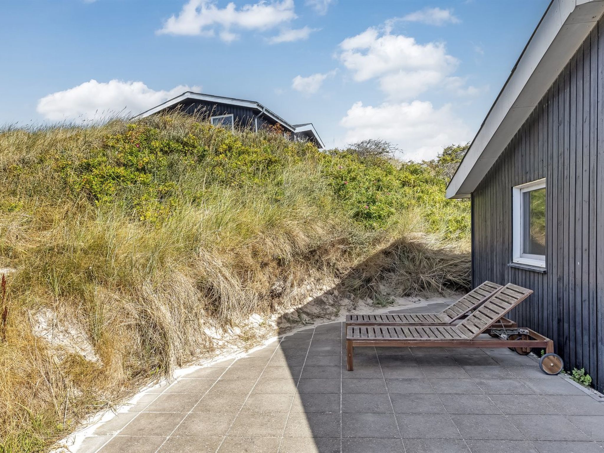 Een houten terras met een lounge stoel, een stenen pad en een gebouw met een schuin dak.