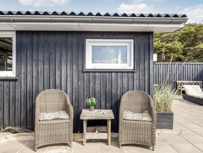 A small outdoor seating area with two wicker chairs and a table, a window, and a dark wooden wall.