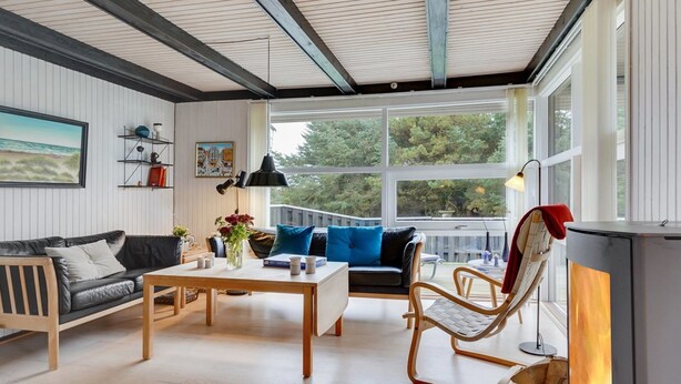 Un salon chaleureux avec une cheminée, des meubles en bois et de grandes fenêtres donnant sur l’extérieur.