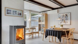 Un salon moderne avec un poêle à bois, un coin repas comprenant une table et des chaises, et un grand tableau abstrait accroché au mur.