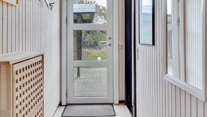 Un couloir avec une porte donnant sur un espace extérieur, une petite fenêtre et un carillon.