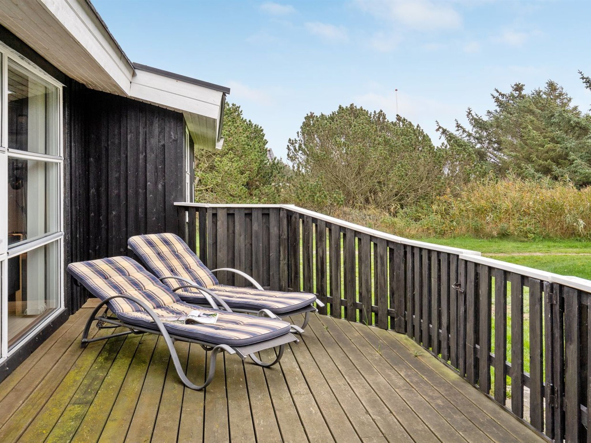 A wooden deck with two lounge chairs and a window overlooking a grassy area.