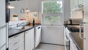 Une cuisine moderne avec des meubles blancs, un plan de travail noir, une fenêtre et un four à micro-ondes.