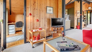 Een gezellige woonkamer met houten wanden, een televisie, een salontafel met een spel en een rode bank.