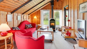 Een gezellig chaletinterieur met houten inrichting, een rode bank, een tafel met lamp, een open haard en een televisie.