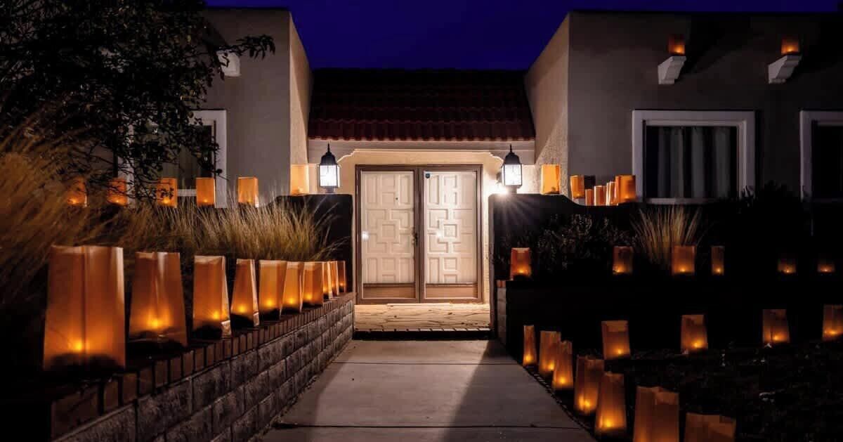 A building entrance with a pathway leading to a double door, surrounded by tall, illuminated lanterns.