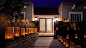 Une entrée d’immeuble avec un chemin menant à une double porte, le tout bordé de hautes lanternes illuminées.