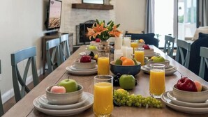 Une table à manger dressée avec des assiettes, des bols et des verres de jus d’orange, entourée de chaises.