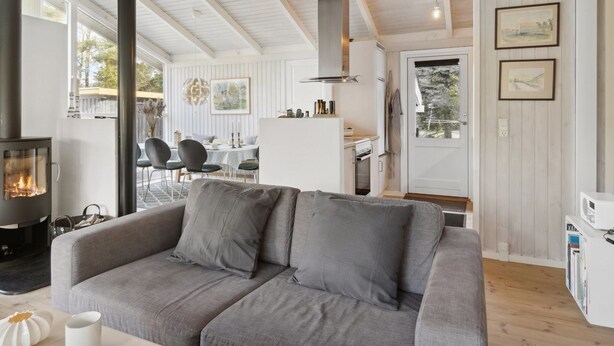 Ein gemütliches Wohnzimmer mit grauem Sofa, Kamin und einem Essbereich mit Tisch und Stühlen.