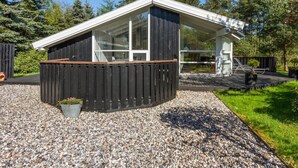 Eine moderne Holzhütte mit großem Panoramafenster, einer Holzterrasse und einem Schotterweg.