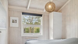 Ein Schlafzimmer mit einem großen Bett, einem Fenster mit Blick auf Bäume, einer Pendelleuchte und einer Heizung.