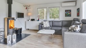 Ein modernes Wohnzimmer mit Kamin, grauem Sofa, weißem Couchtisch und großen Fenstern.