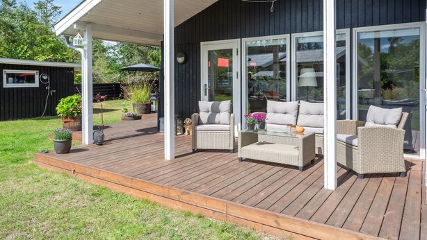 Eine überdachte Terrasse im Freien mit Korbmöbeln und einer Glastür, die in einen Garten führt.