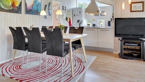 Una cocina moderna con armarios blancos, una zona de comedor con una mesa blanca y sillas negras, y un televisor de pantalla plana grande.