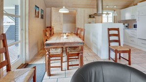 A spacious dining area with a wooden table and chairs, a kitchen with white cabinets, and a large window providing natural light.