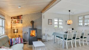 A cozy living room with a wood-burning stove, a dining area with white chairs, and a bookshelf filled with books.