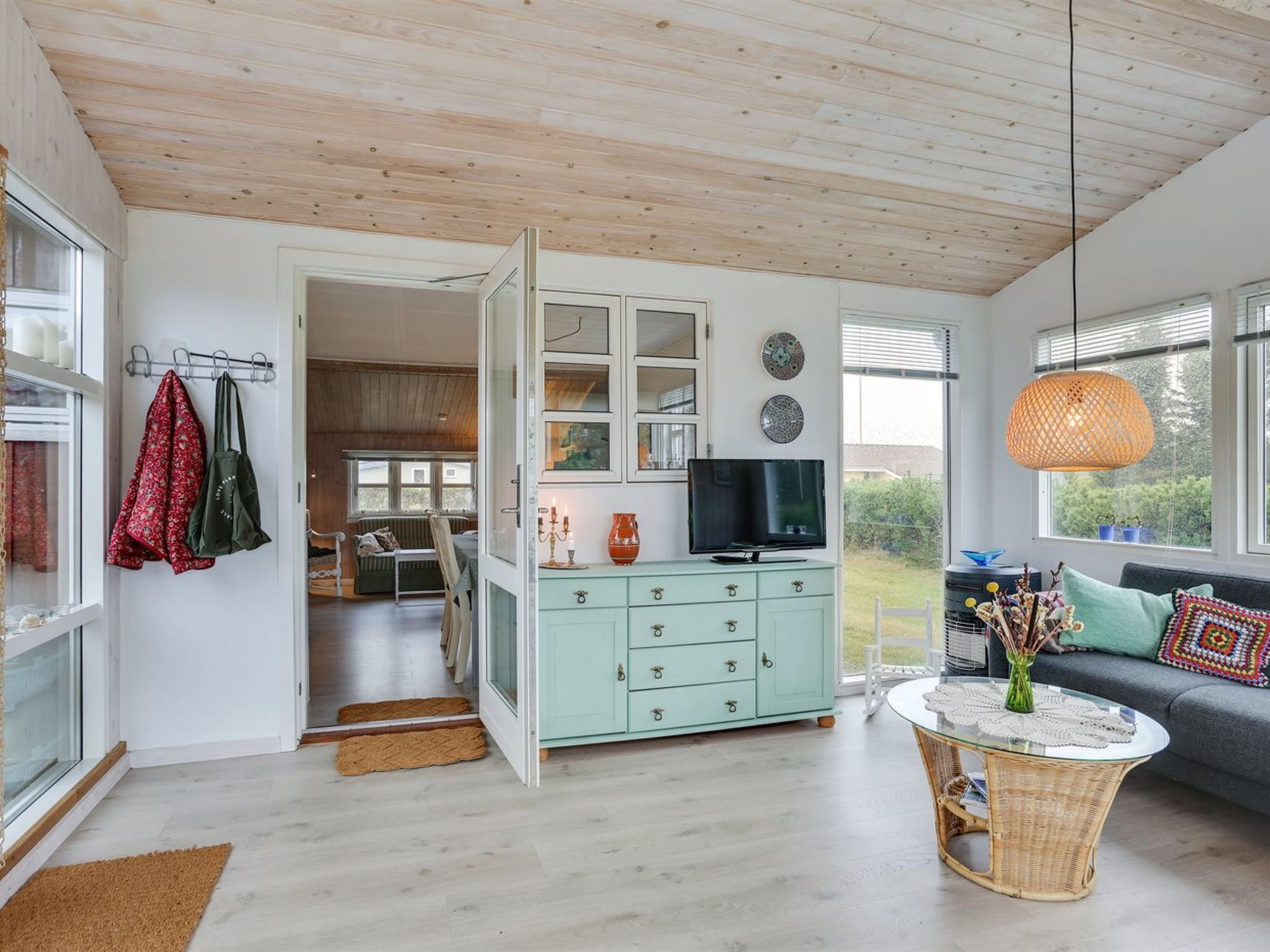 Un salon moderne avec un meuble turquoise, un téléviseur et une table basse en osier.