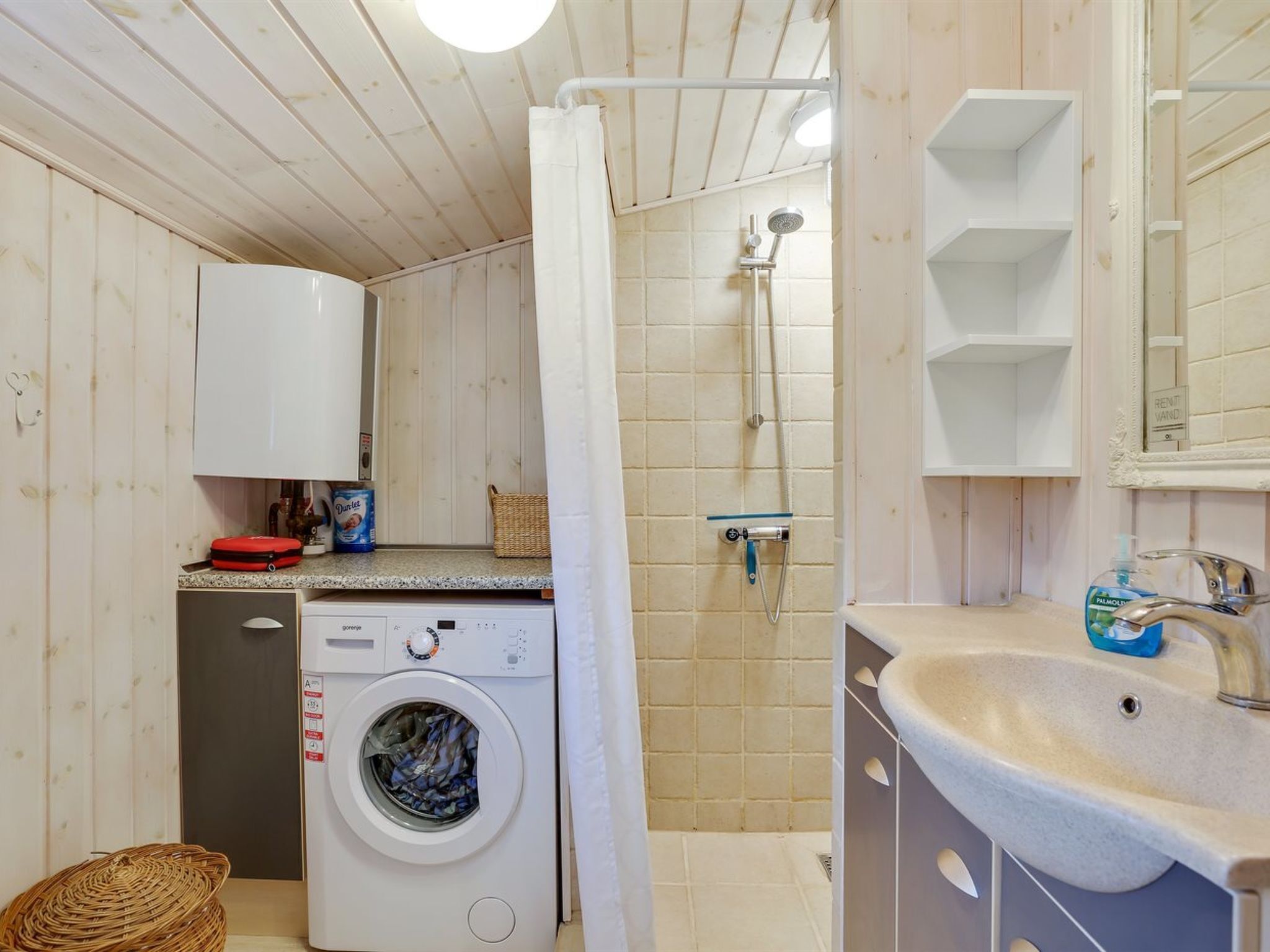 Een kleine badkamer met een wasmachine, douche en wastafel.