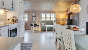 A cozy kitchen with wooden beams, a dining area with white chairs, and a large window providing natural light.