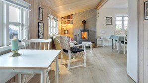 A cozy room with a wooden ceiling, a fireplace, a bookshelf, and a dining area with a table and chairs.