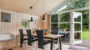 A modern kitchen with wooden walls, a dining area with black chairs, and a large sliding glass door leading to an outdoor patio. - "Femke" - 250m to the fjord by Interhome (Storvorde)
