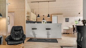 A modern kitchen with wooden cabinets, a central island with bar stools, pendant lighting, and a black stove. - "Femke" - 250m to the fjord by Interhome (Storvorde)