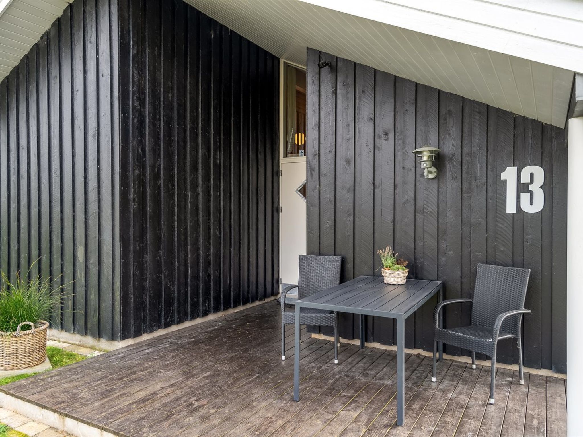 Een overdekt terras met een donkere houten wand, een bord met het nummer '13' en een kleine tafel met stoelen.