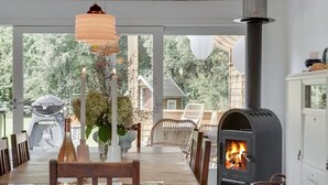 A cozy indoor space with a wood-burning stove, a dining area with chairs and a table, and a view of the outdoors.