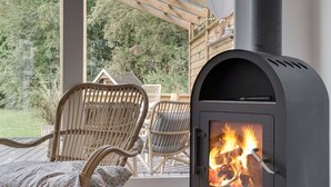 A wood-burning stove in a covered outdoor seating area with wicker chairs and a view of a garden.